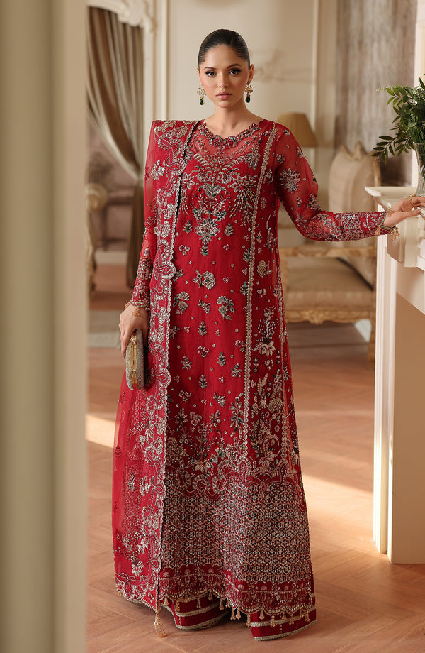 Woman in a Surkh Gul red and gold traditional outfit standing in an elegant room.