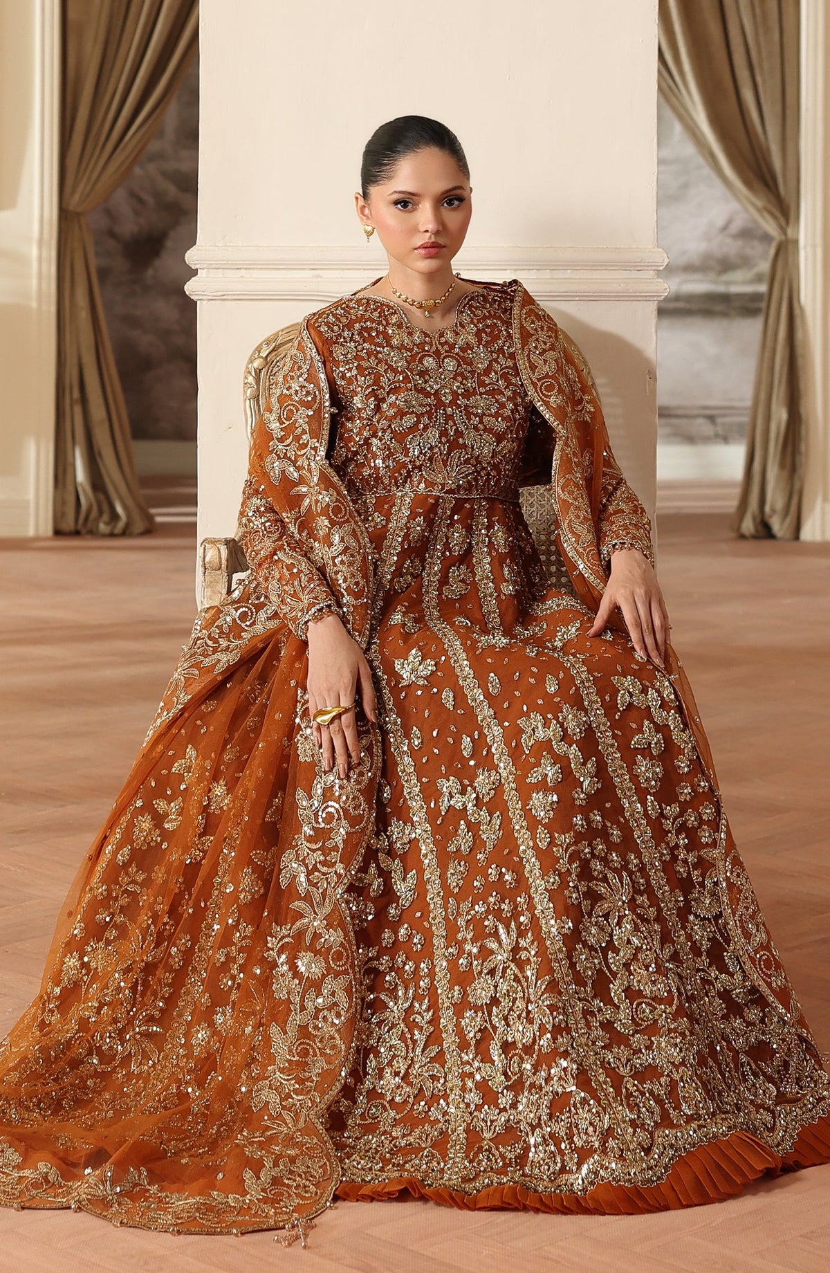 Woman in a traditional embroidered outfit sitting in a decorated room.